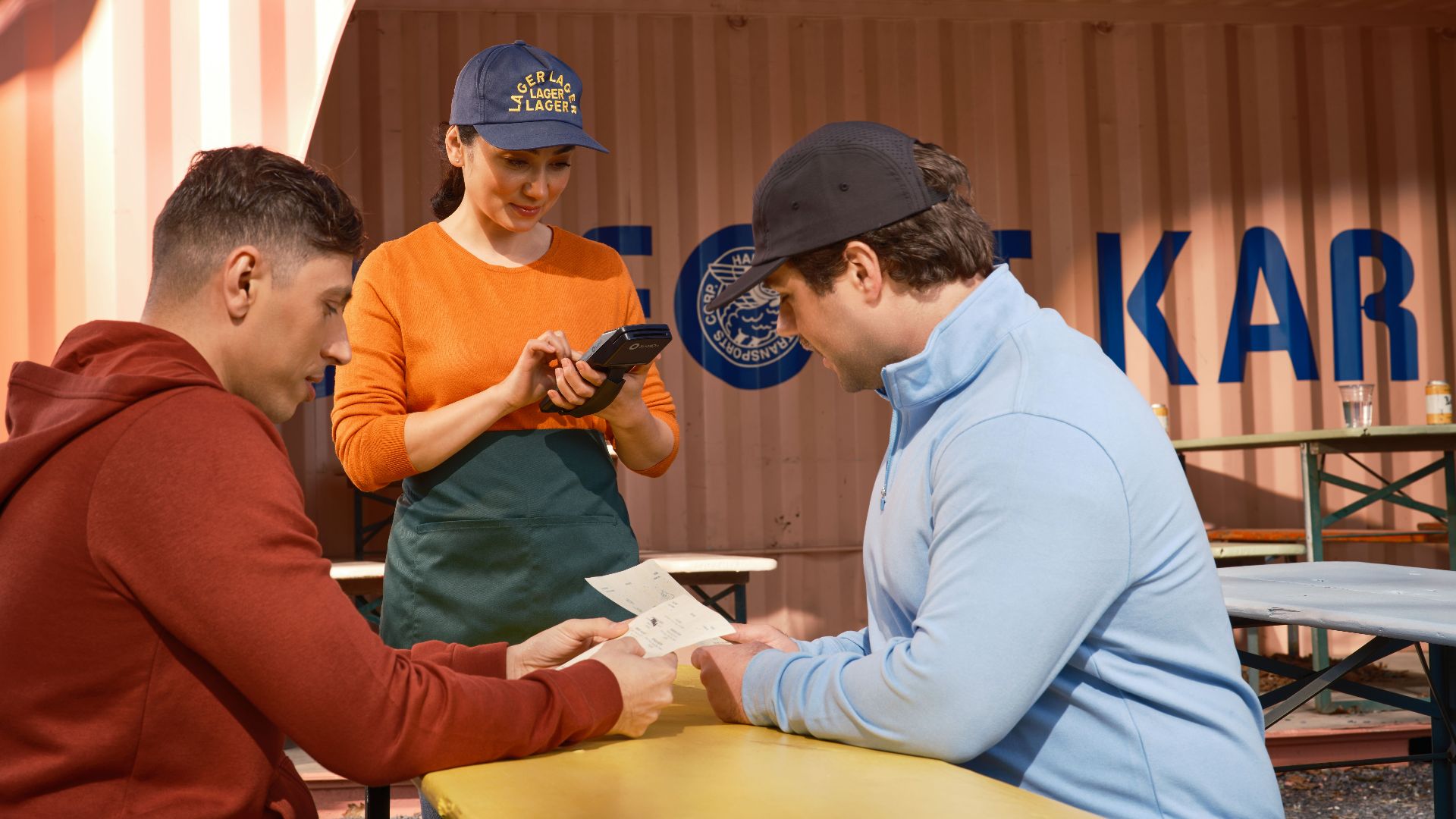 A restaurant staff member takes orders using a handheld device in an outdoor café setting.