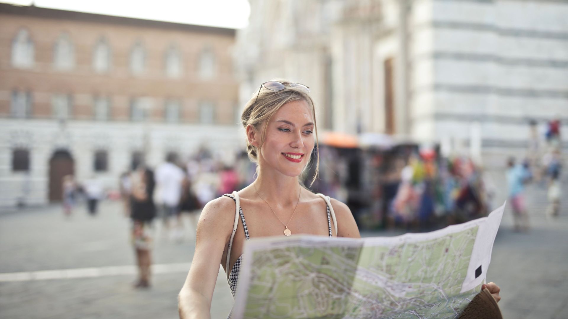 Smiling woman holding a map, discovering city landmarks under the sun. Perfect for travel and tourism concepts.