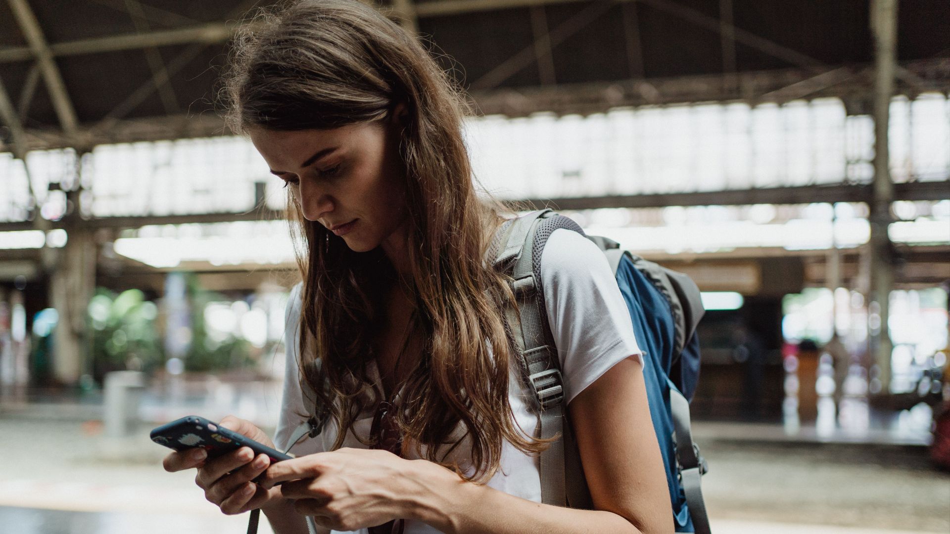 A young woman checks her smartphone while traveling at a train station.