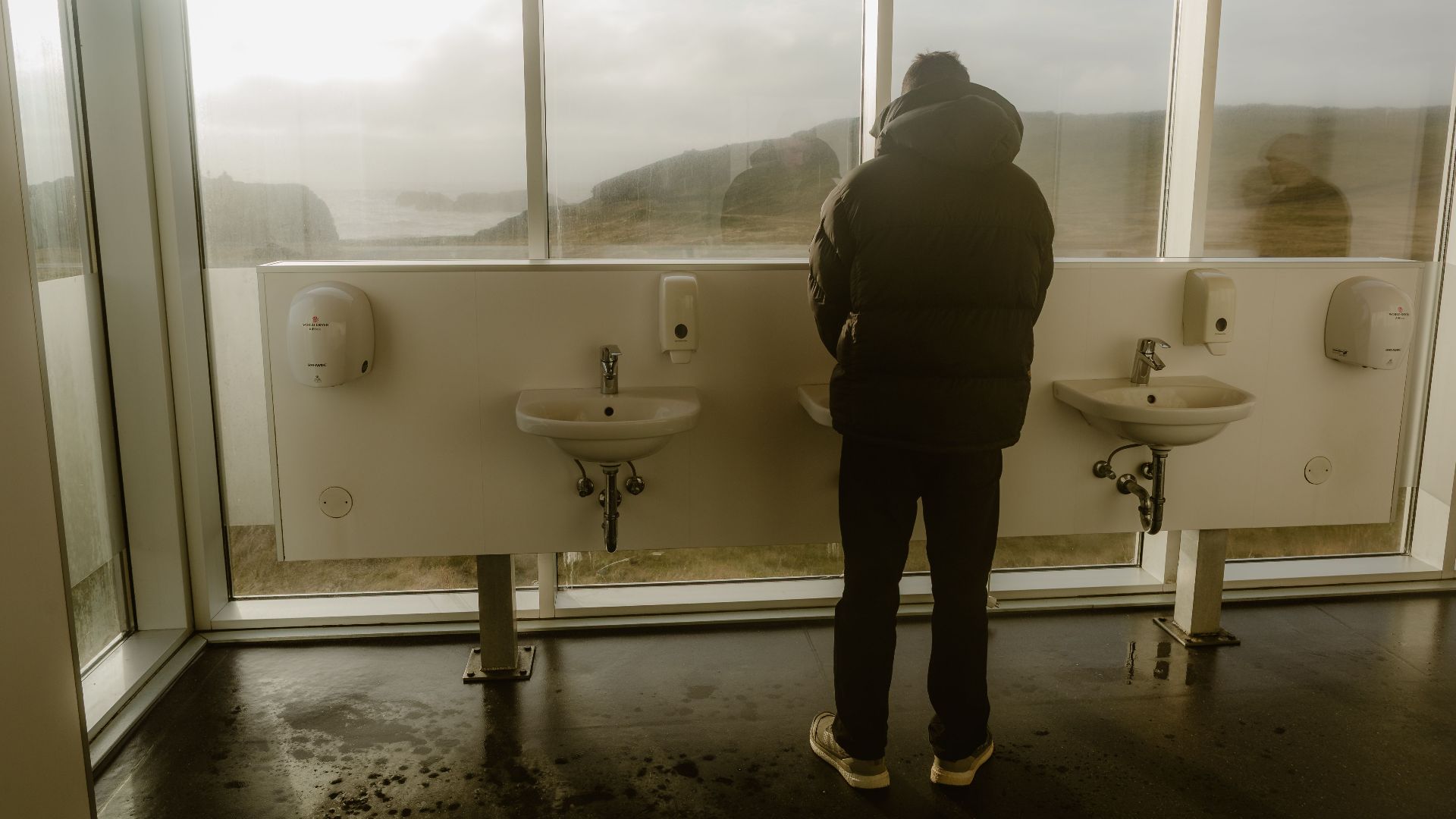 A person stands in a modern restroom with large windows offering a scenic, misty view outside.
