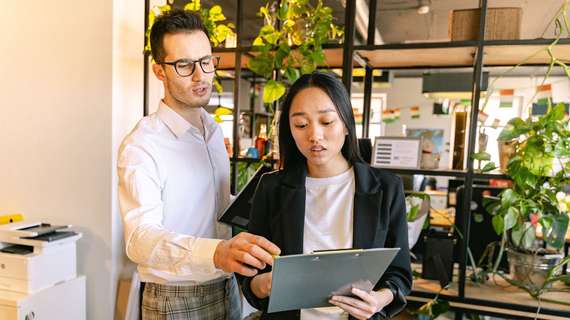 A man and woman collaborating on a project in a modern office setting with plants.