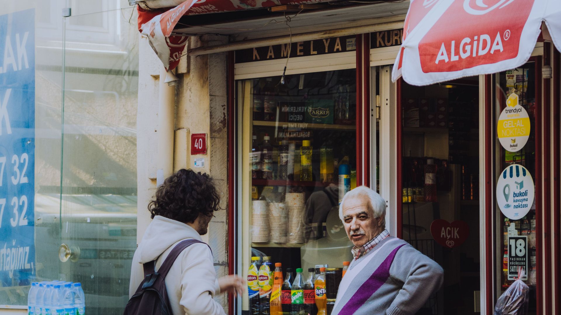 Elderly man and adult conversing outside a quaint urban store with local products.