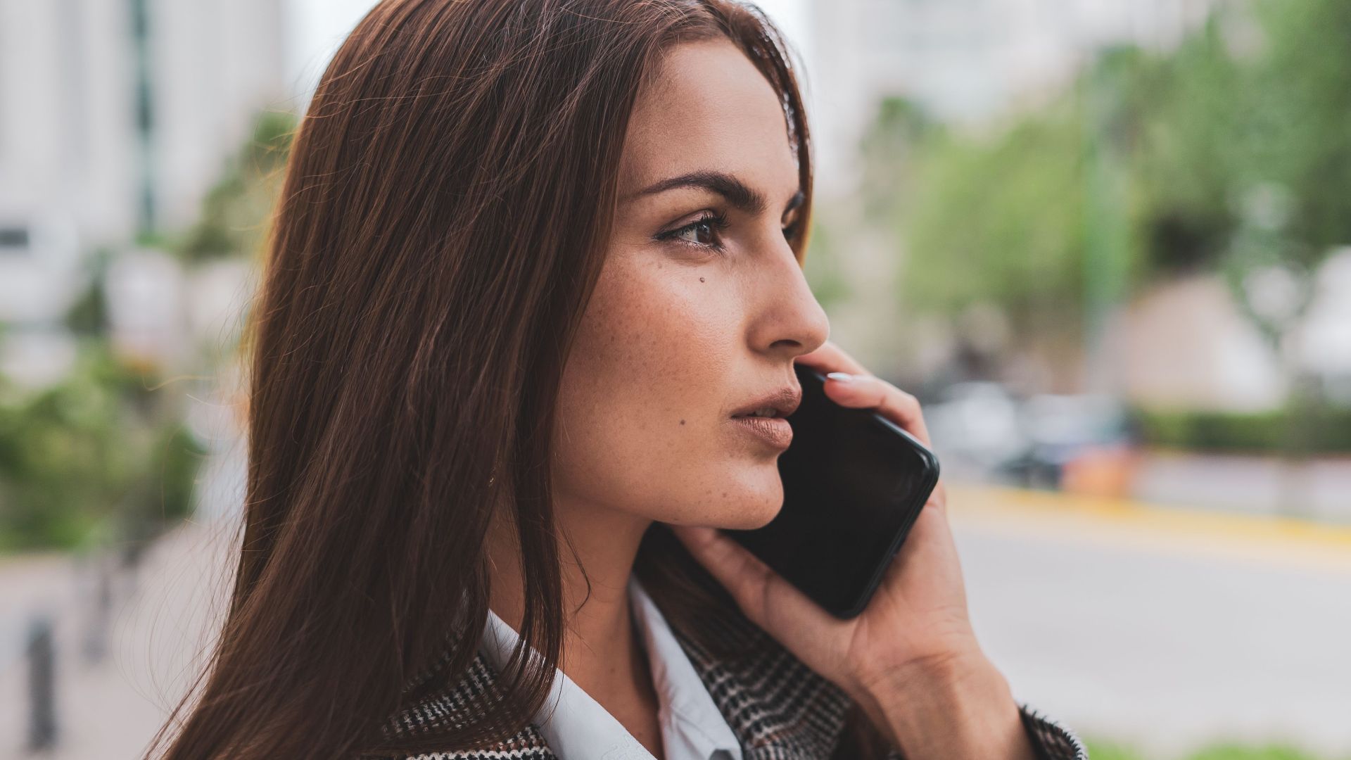 Confident businesswoman with brown hair talking on smartphone outdoors.
