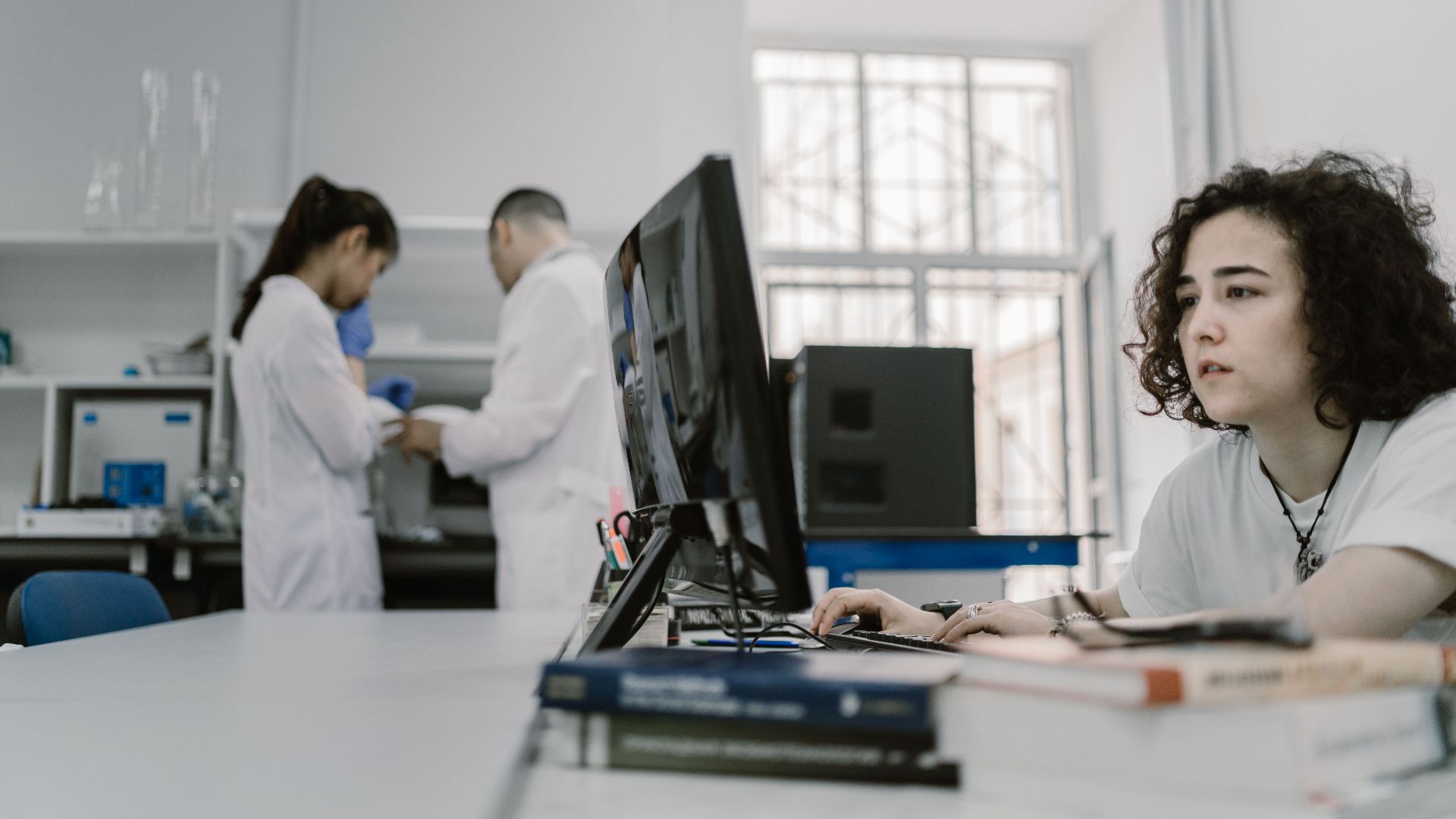 Focused woman working on a computer in a busy laboratory setting, showcasing teamwork and scientific research.