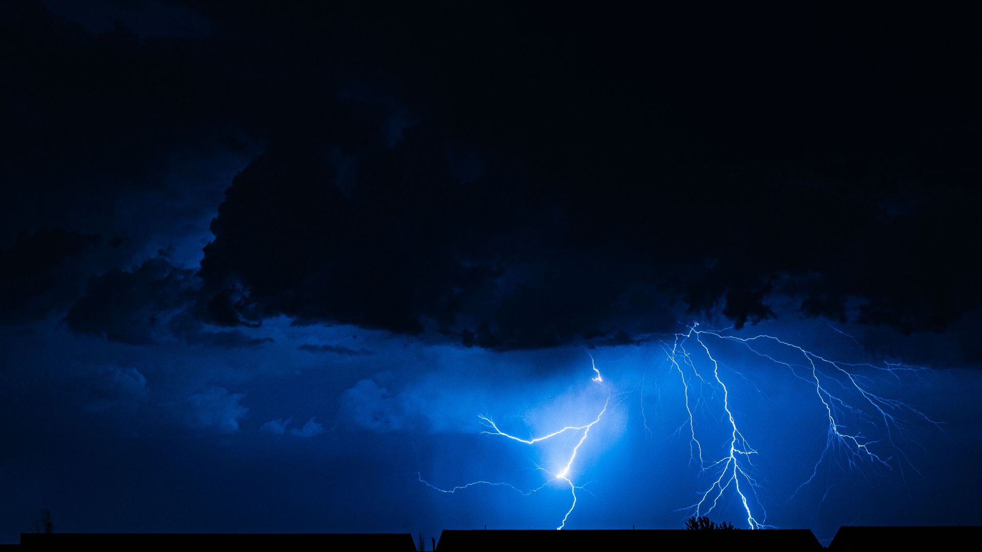 Powerful lightning illuminates the night sky during a storm, casting silhouettes over city rooftops.