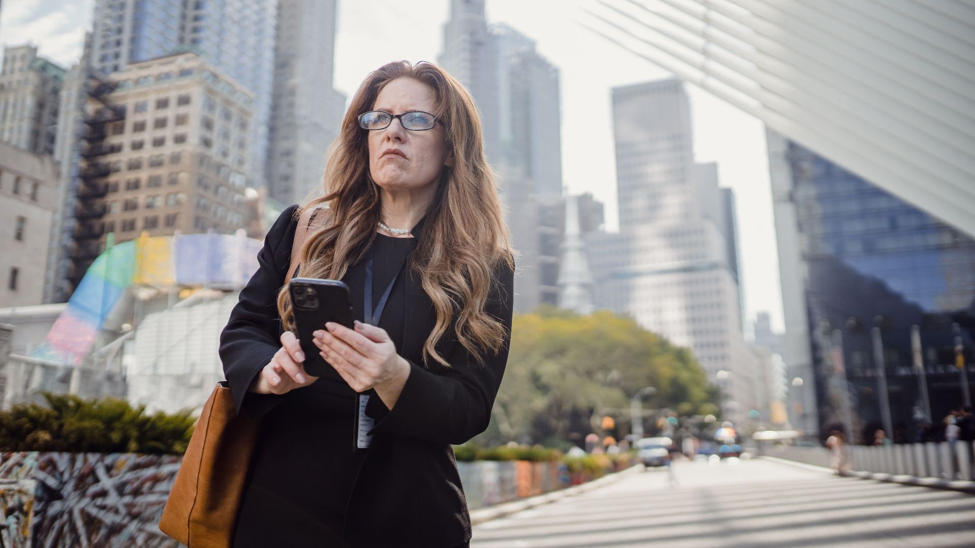 Confident woman with smartphone walking amidst modern skyscrapers. Urban business concept.