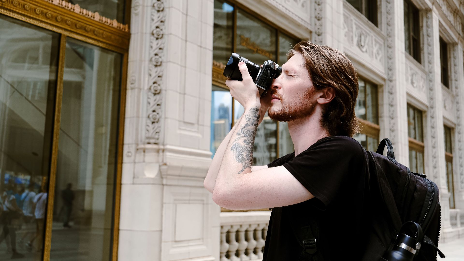 Young photographer with tattoos taking pictures outside a historic urban building. Ideal for creative lifestyle and travel themes.