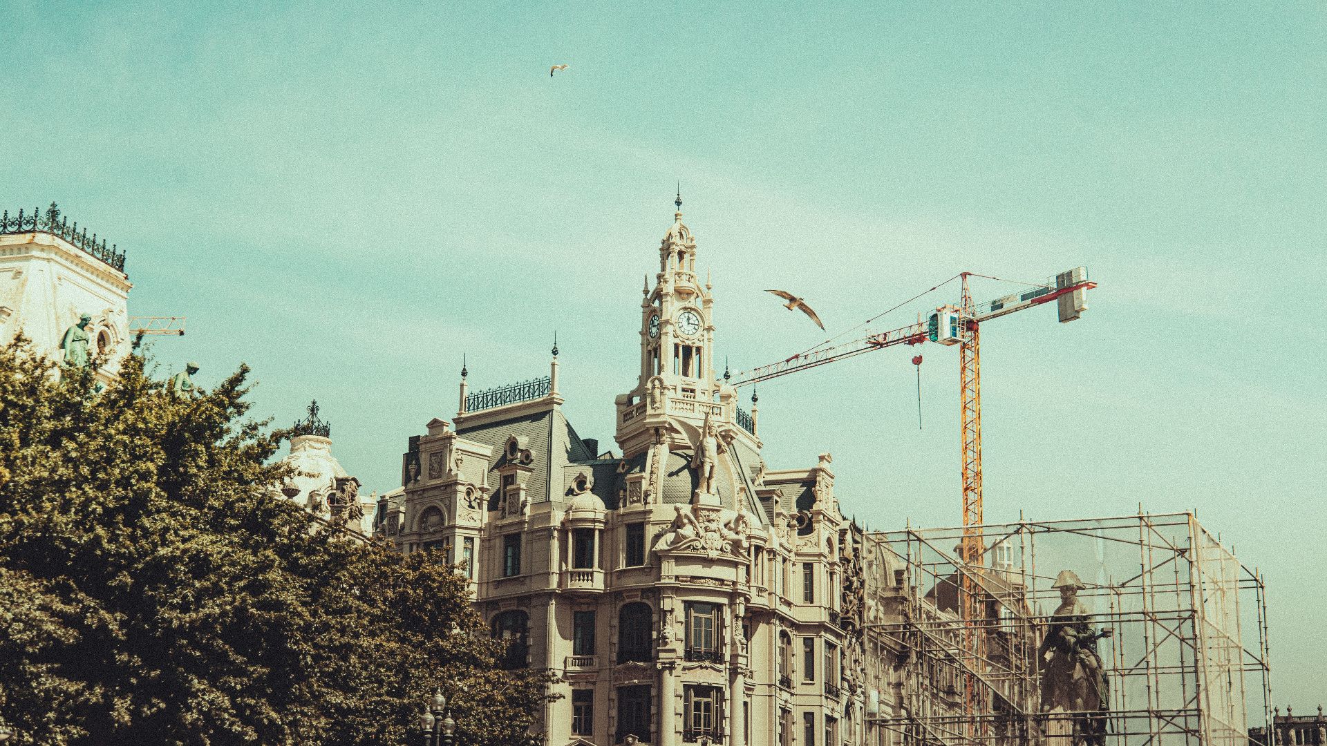 View of a historic European building beside a crane and scaffolding under a blue sky.
