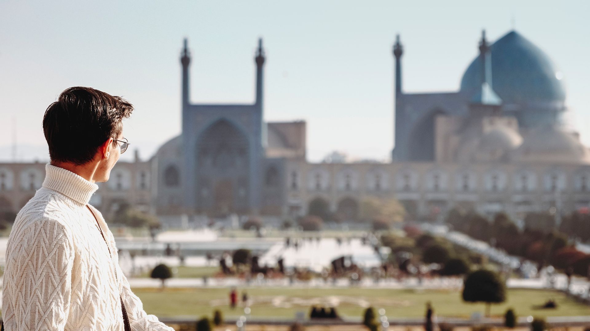 A man gazing at the iconic Sheikh Lotfollah Mosque in Isfahan, Iran, during a sunny day.