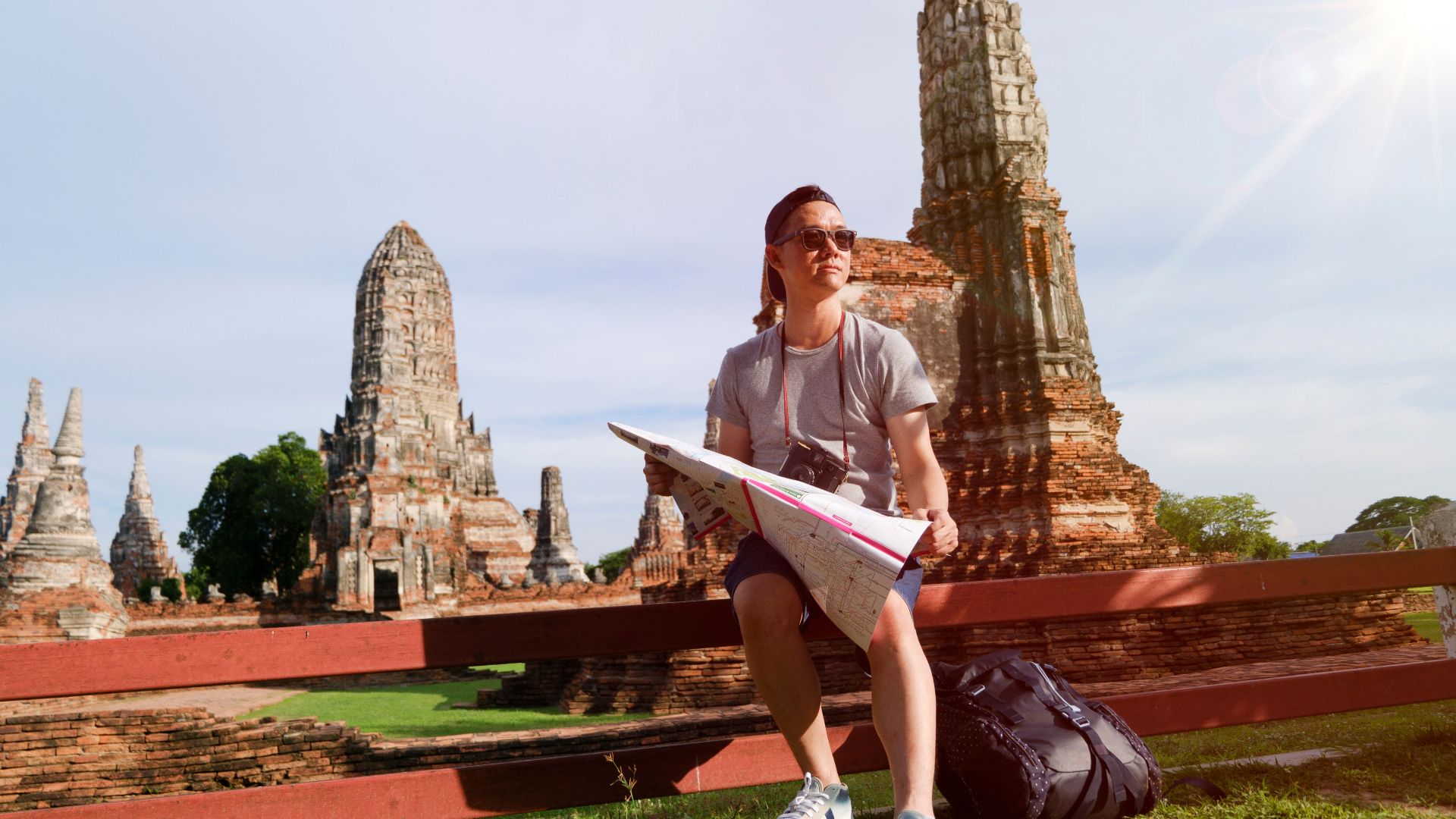 Man studying map amidst ancient temple ruins in Thailand, highlighting travel and exploration.