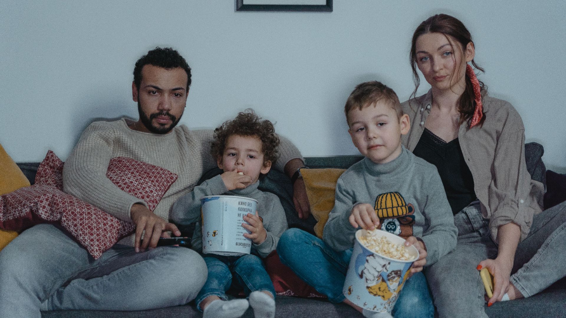 Family of four enjoying a cozy movie night with popcorn on the sofa.