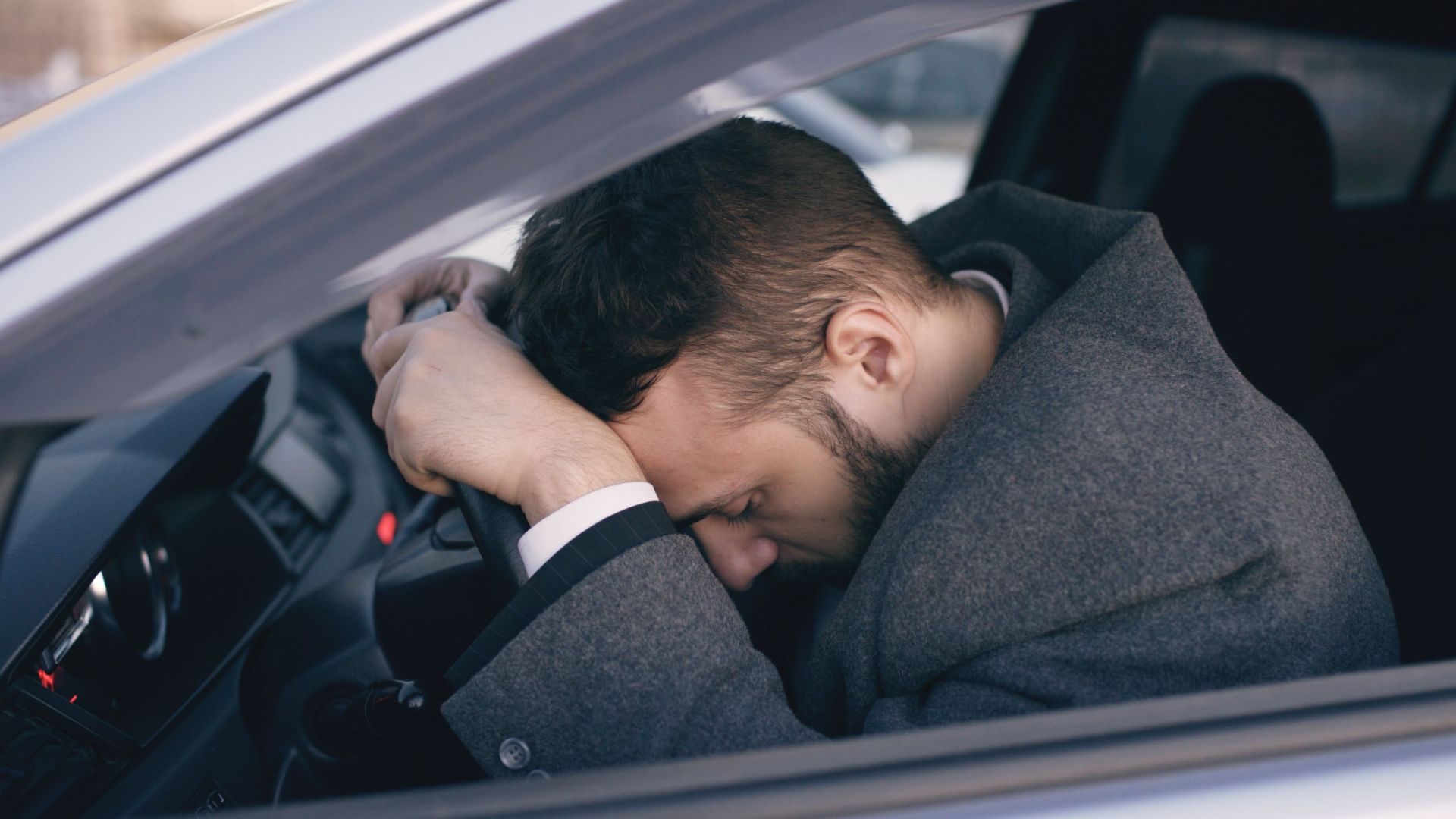Man in car showing stress with head on steering wheel, highlighting emotional fatigue.
