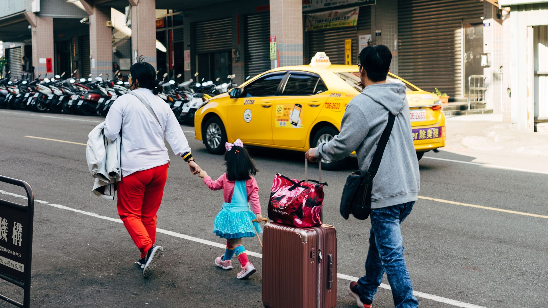 A family walks with luggage past a taxi in Taipei, showcasing urban travel life.