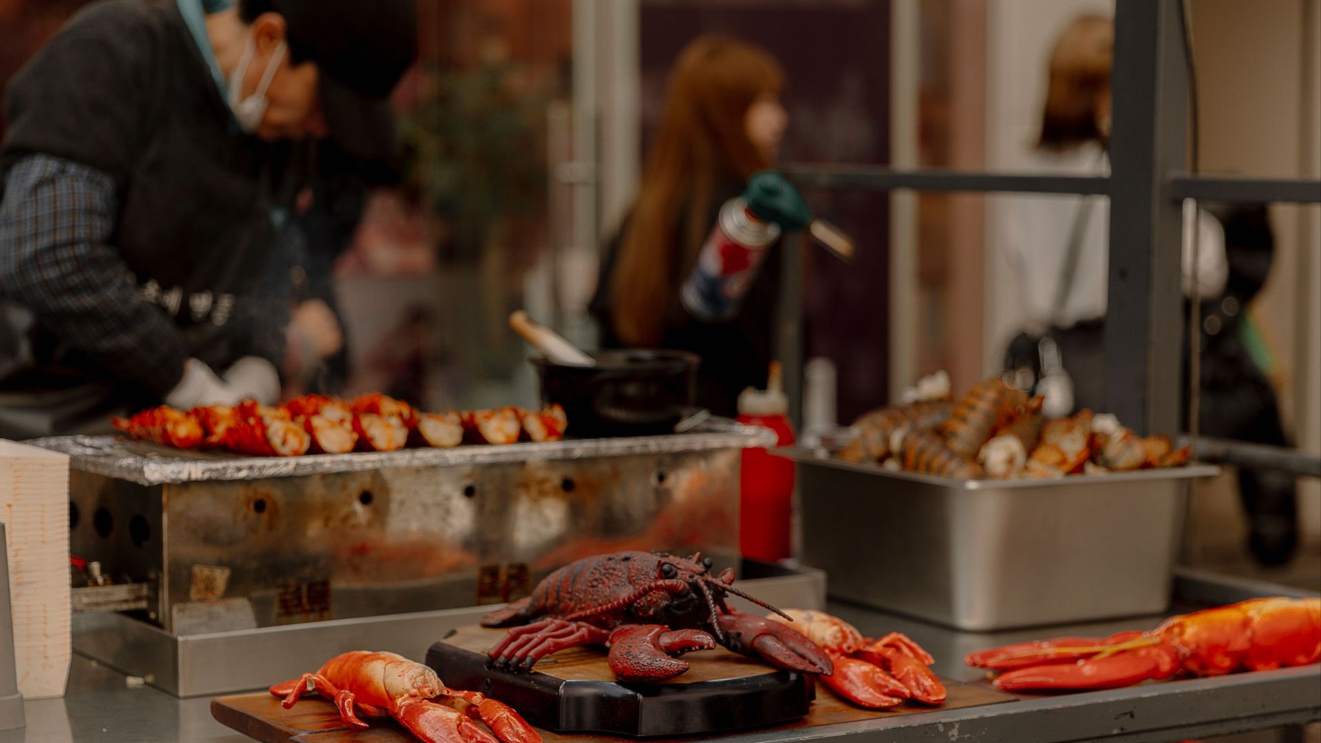 Lobsters being grilled at a bustling outdoor market food stall.