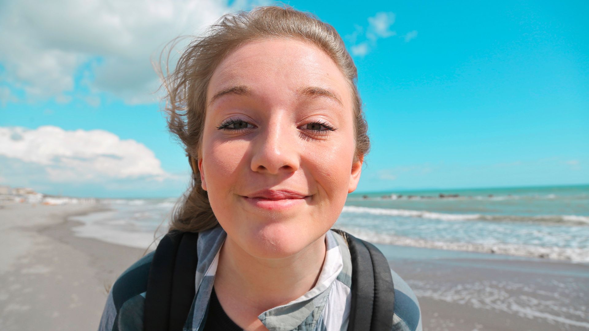 Cheerful woman with backpack on a sunny beach day, enjoying the ocean breeze.