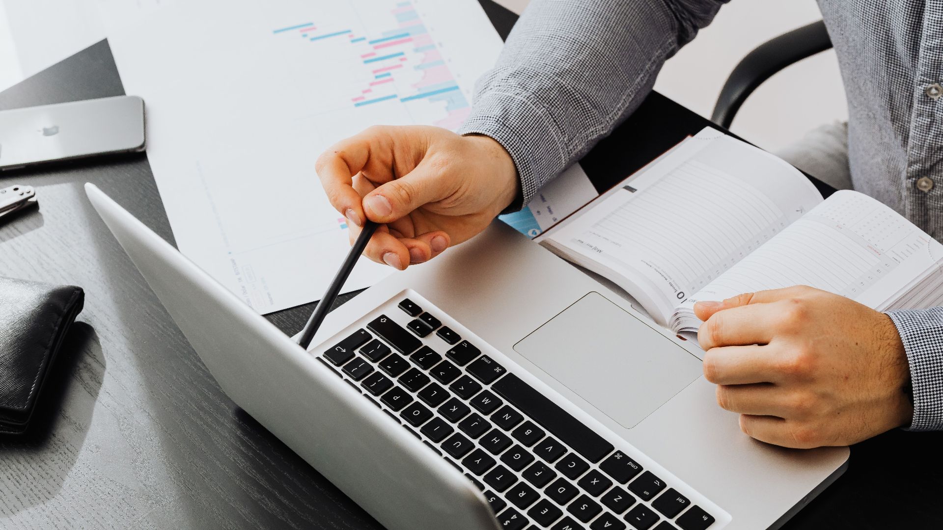Professional using laptop and reviewing documents at office desk for data analysis.