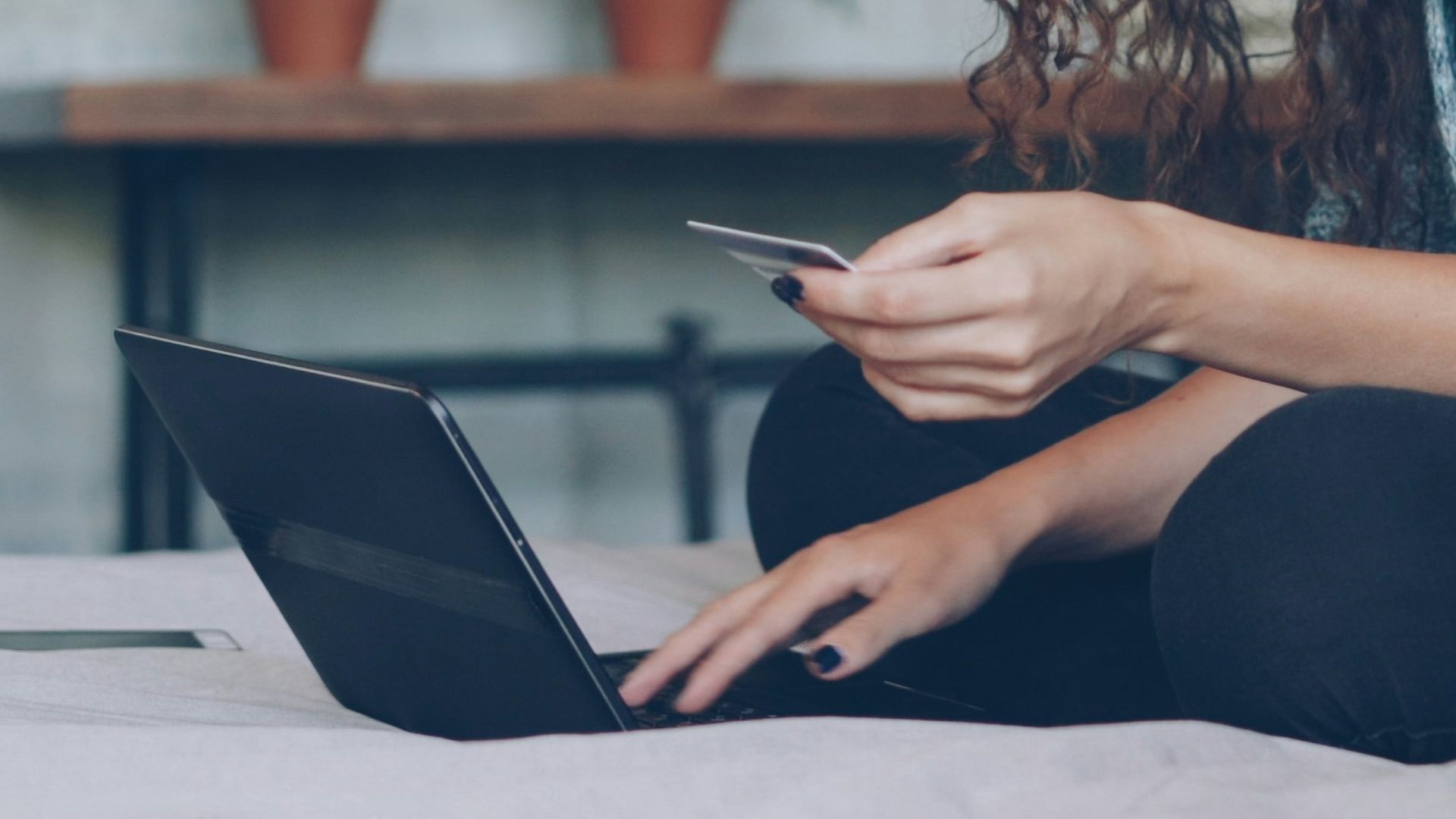 Woman using laptop and credit card on bed.