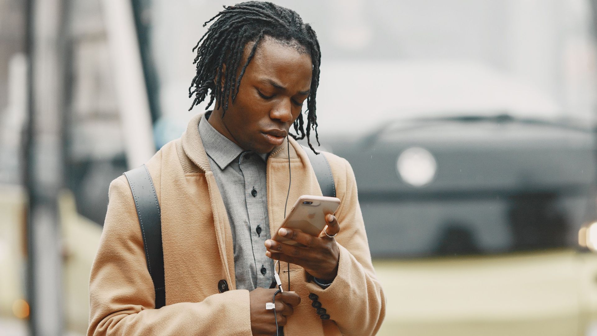 A young man in a coat using his smartphone while standing near a city bus on a winter day.