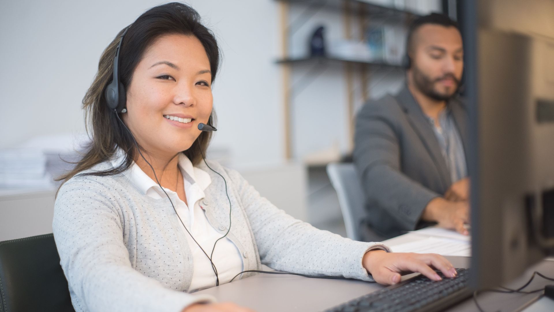 Two call center employees working with headsets in a modern office setting.