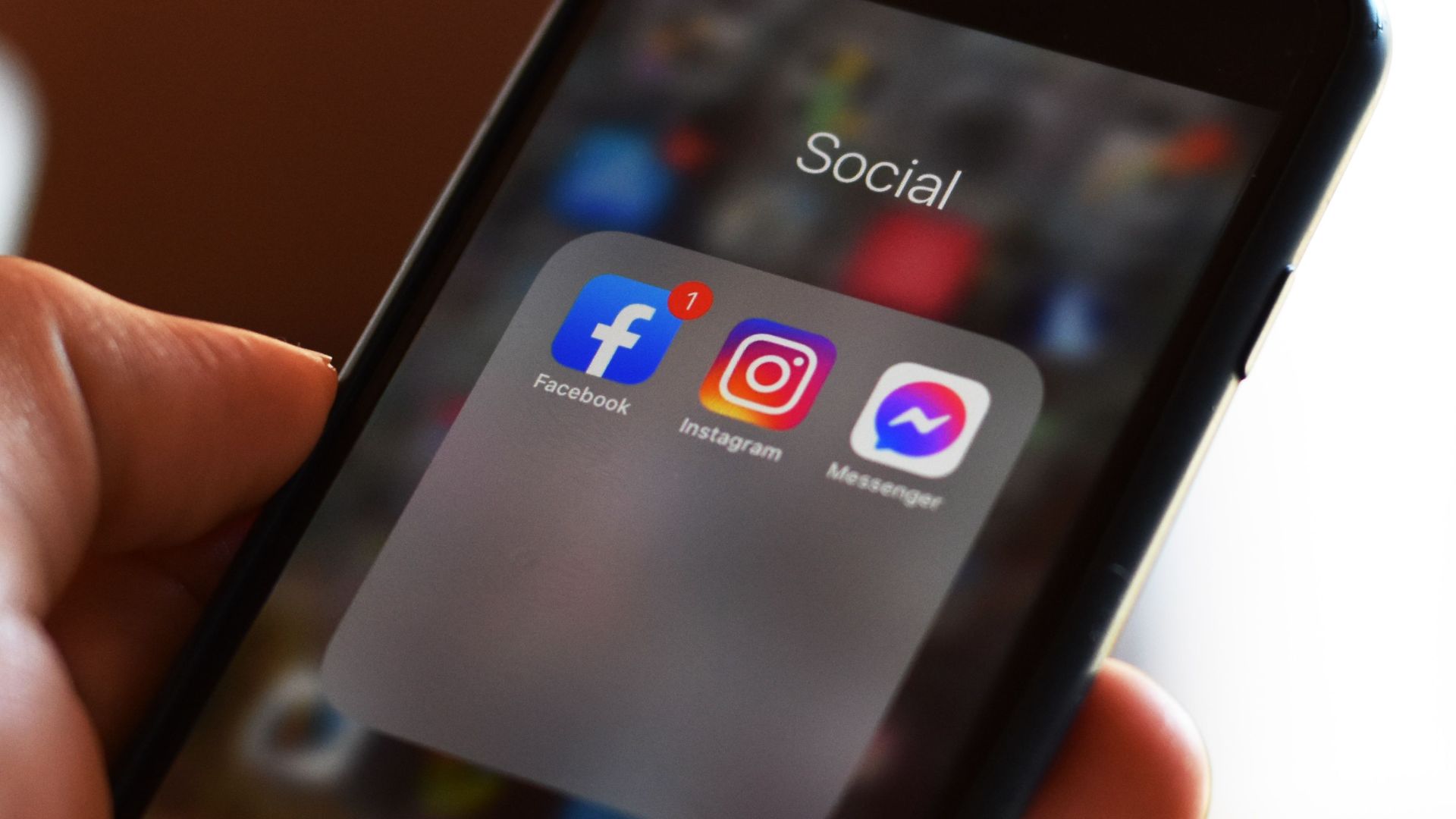 Close-up of hand holding smartphone showing social media apps like Facebook and Instagram.