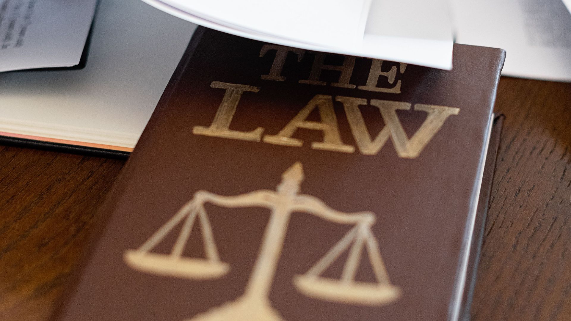 Close-up of a law book with scales icon on a wooden desk covered in papers.