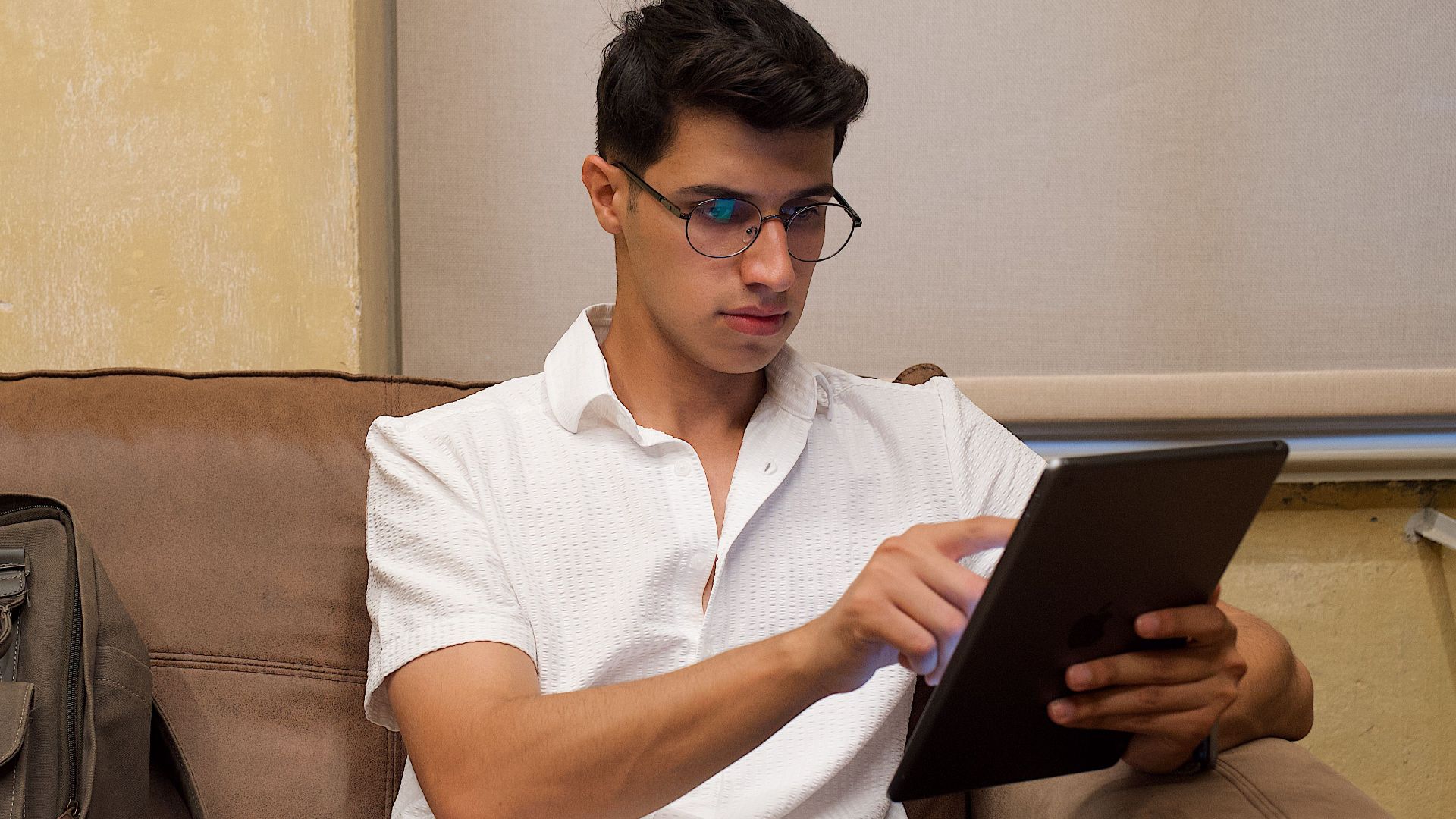 A man sitting on a sofa using a tablet in a relaxed indoor setting.