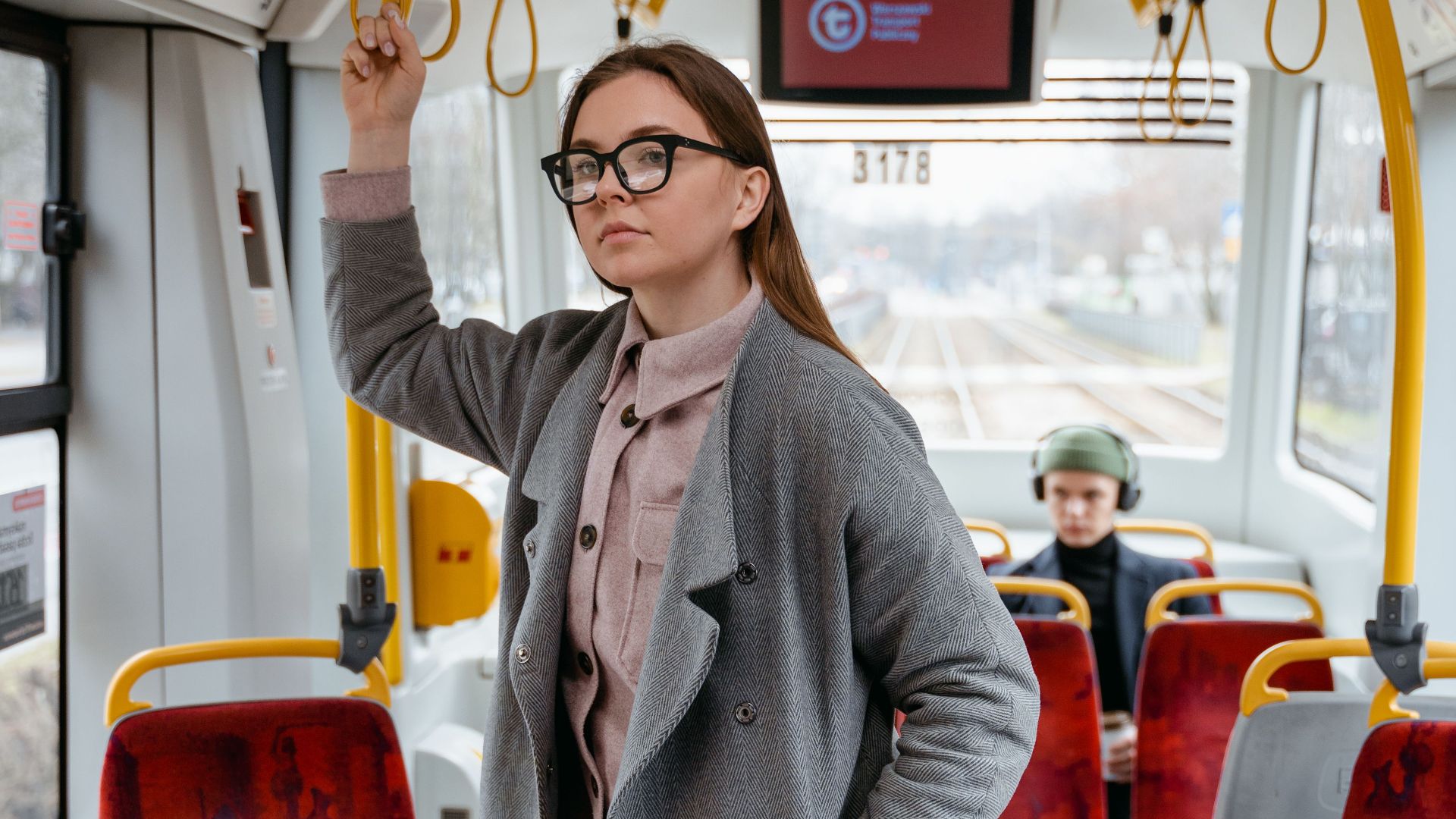 Woman wearing eyeglasses stands confidently in a tram holding a handrail.