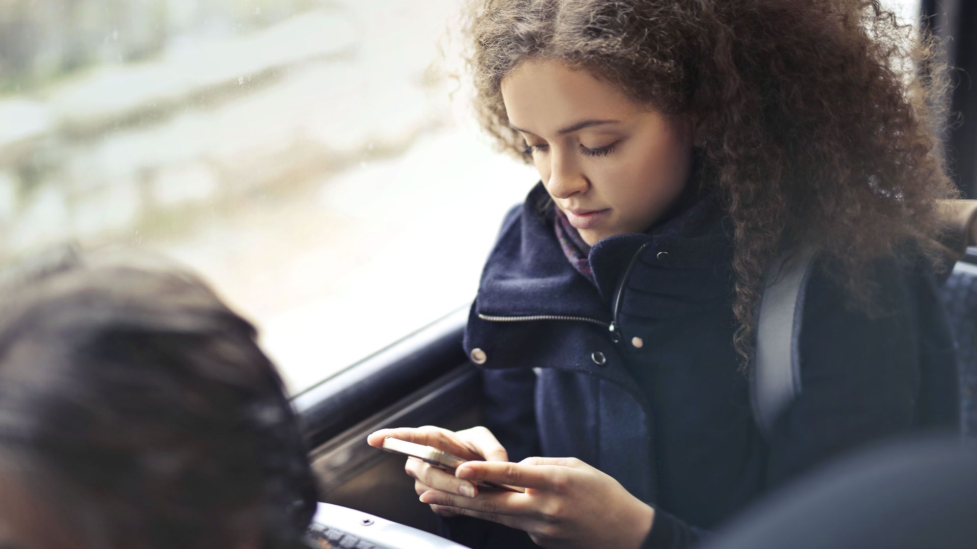 Young woman with curly hair texting on smartphone in public transport.