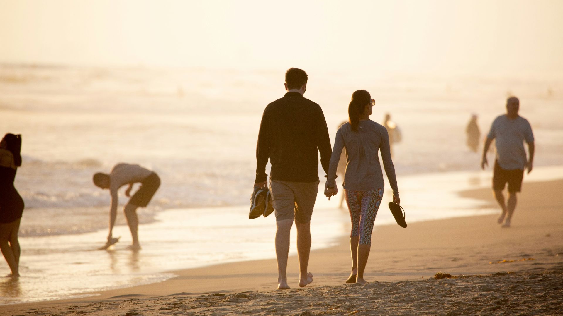 man and woman holding hands while walking on beach during daytime