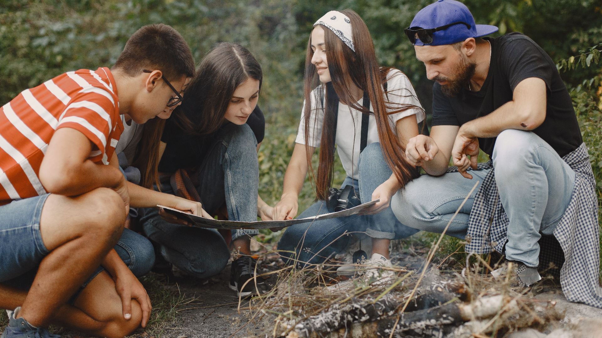 Young friends gathered around a map planning their next outdoor adventure near a campfire.