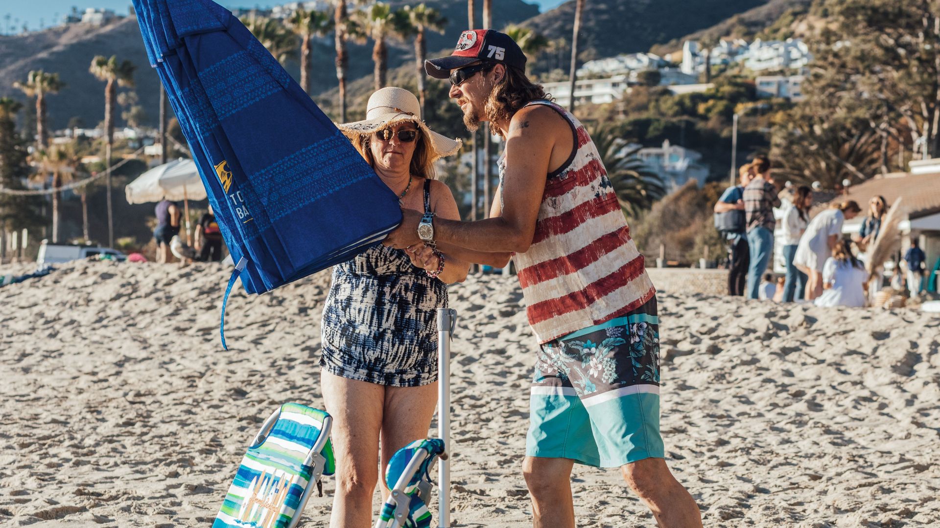A cheerful couple sets up an umbrella on a sunny beach, ready for a fun summer day.