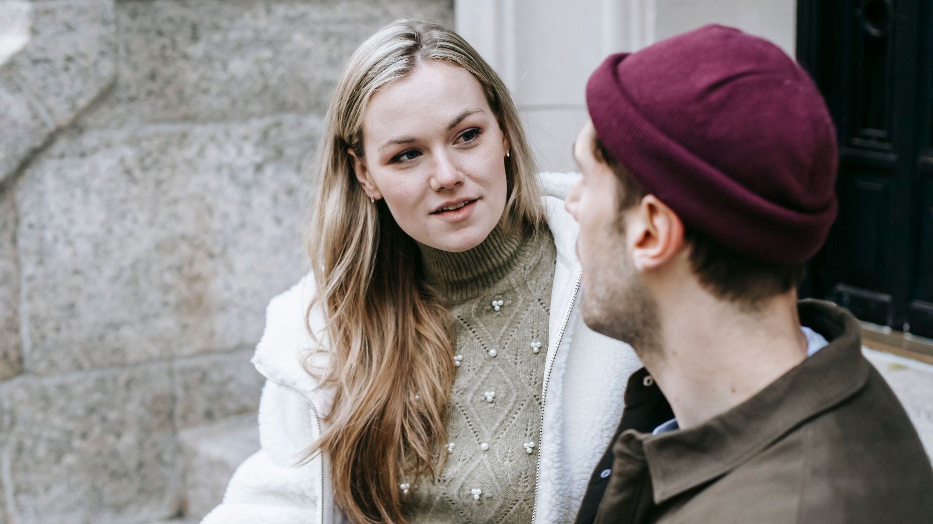 Man and woman talking sitting on steps outside house and having hot beverage in paper cups