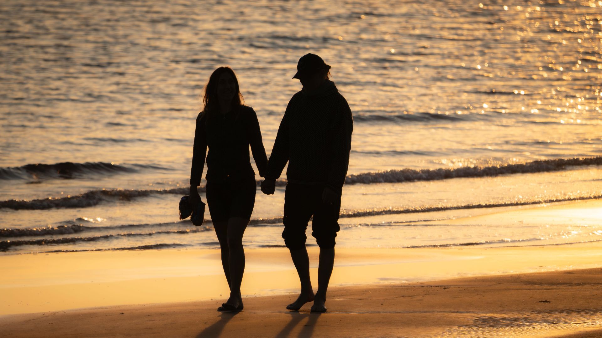Silhouette of a couple walking hand in hand on a sunny beach at sunset.