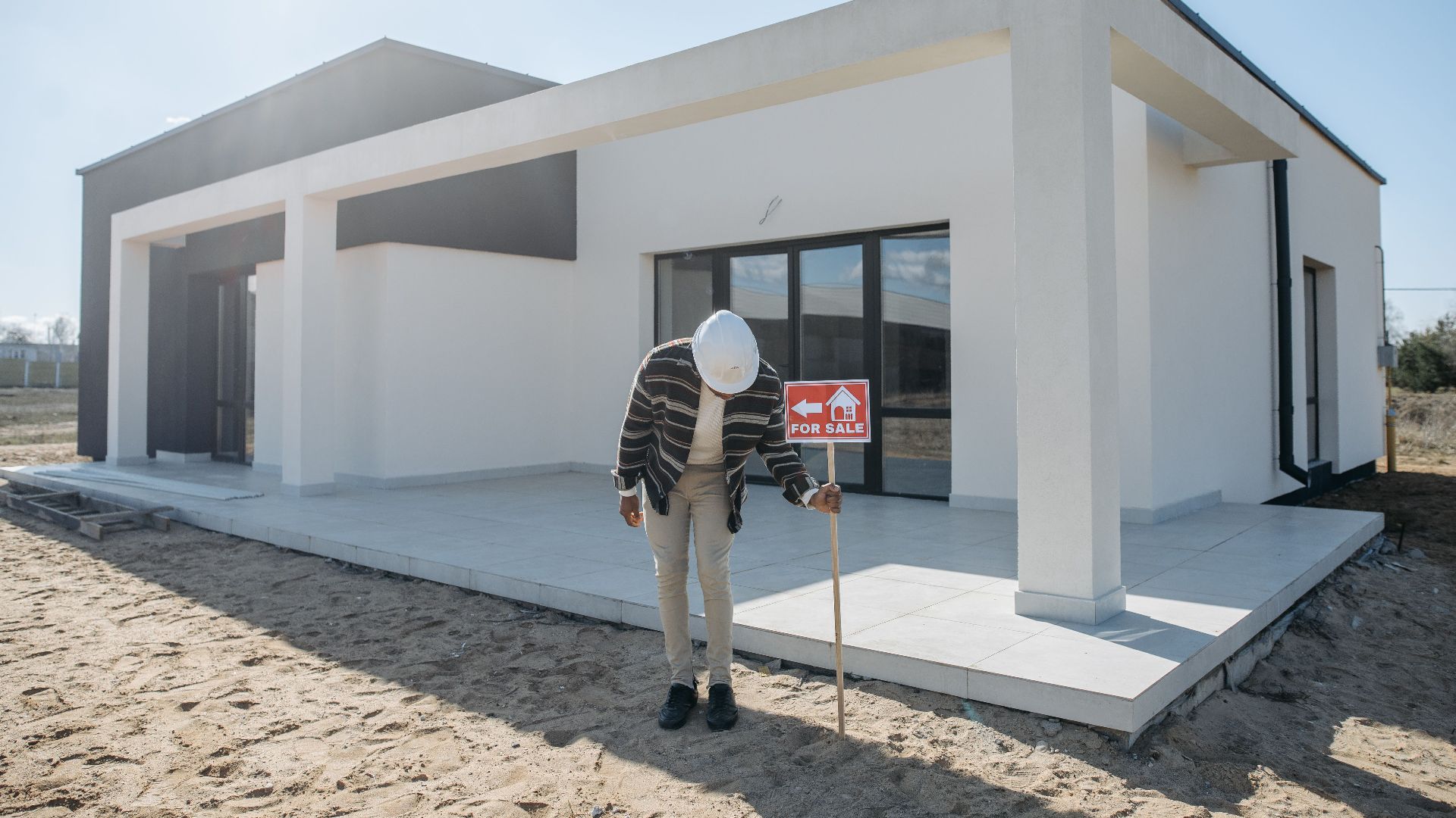Real estate agent with hard hat standing by a modern house for sale.