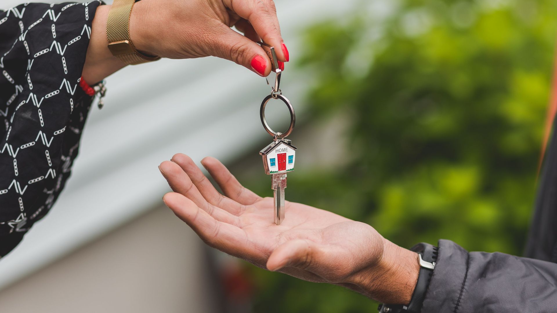Close-up of a hand handing over a key with a house keychain, symbolizing real estate transaction.