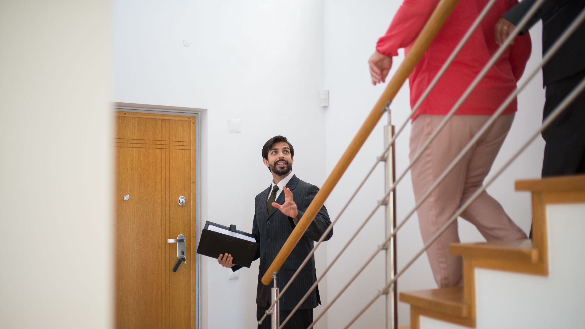 A realtor conducting a house tour with potential buyers on the stairs of a modern home.