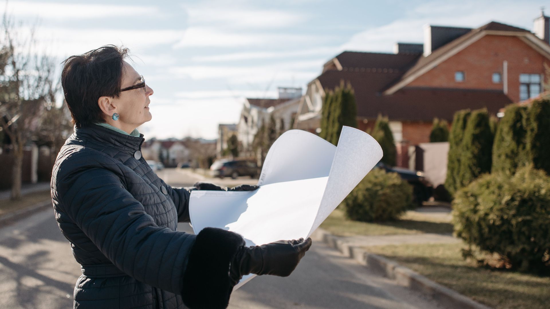 Woman in a blue jacket reviewing architectural plans outdoors on a sunny day.