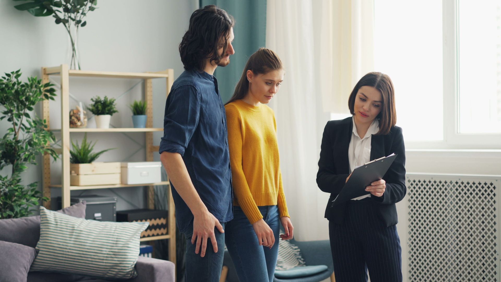 Real estate agent consulting a couple in a modern living room setting, surrounded by indoor plants.