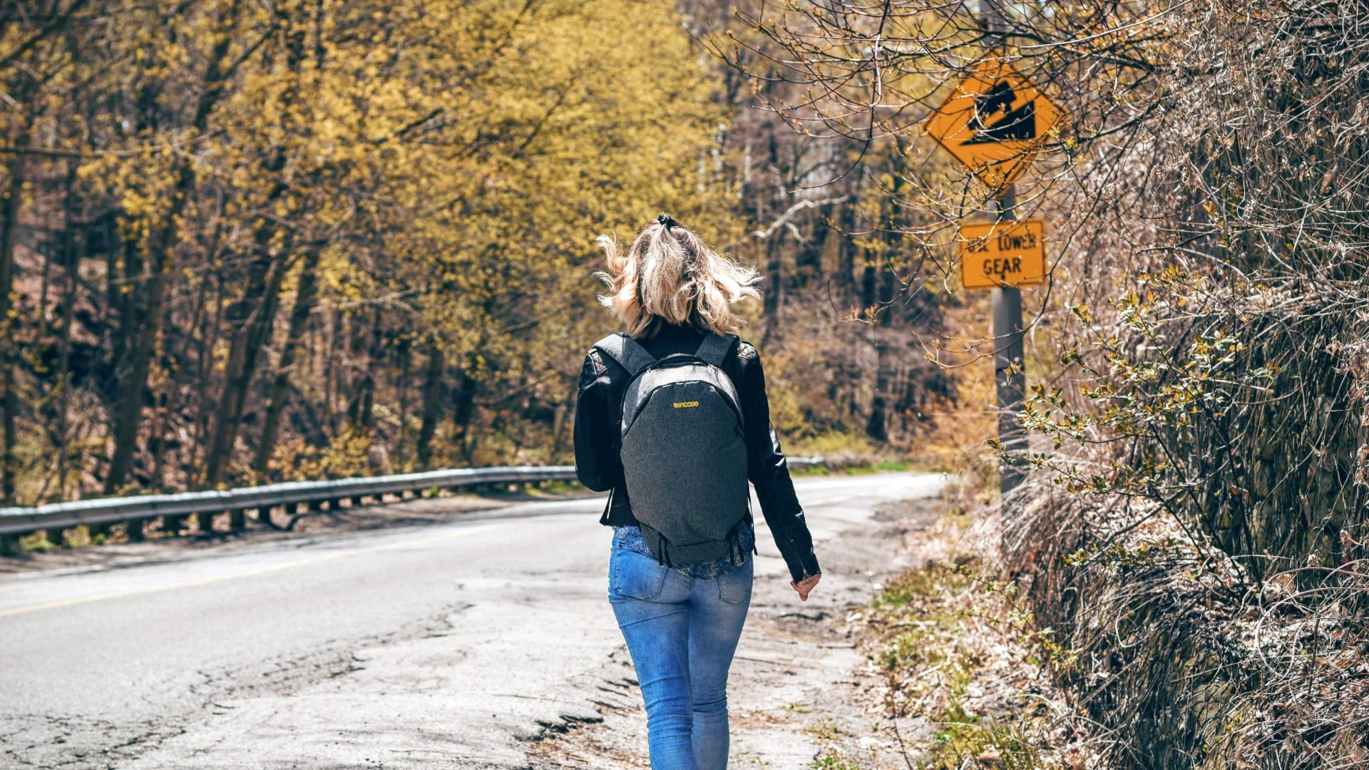 A woman with a backpack walks along a scenic forest road in spring, enjoying an outdoor hike.