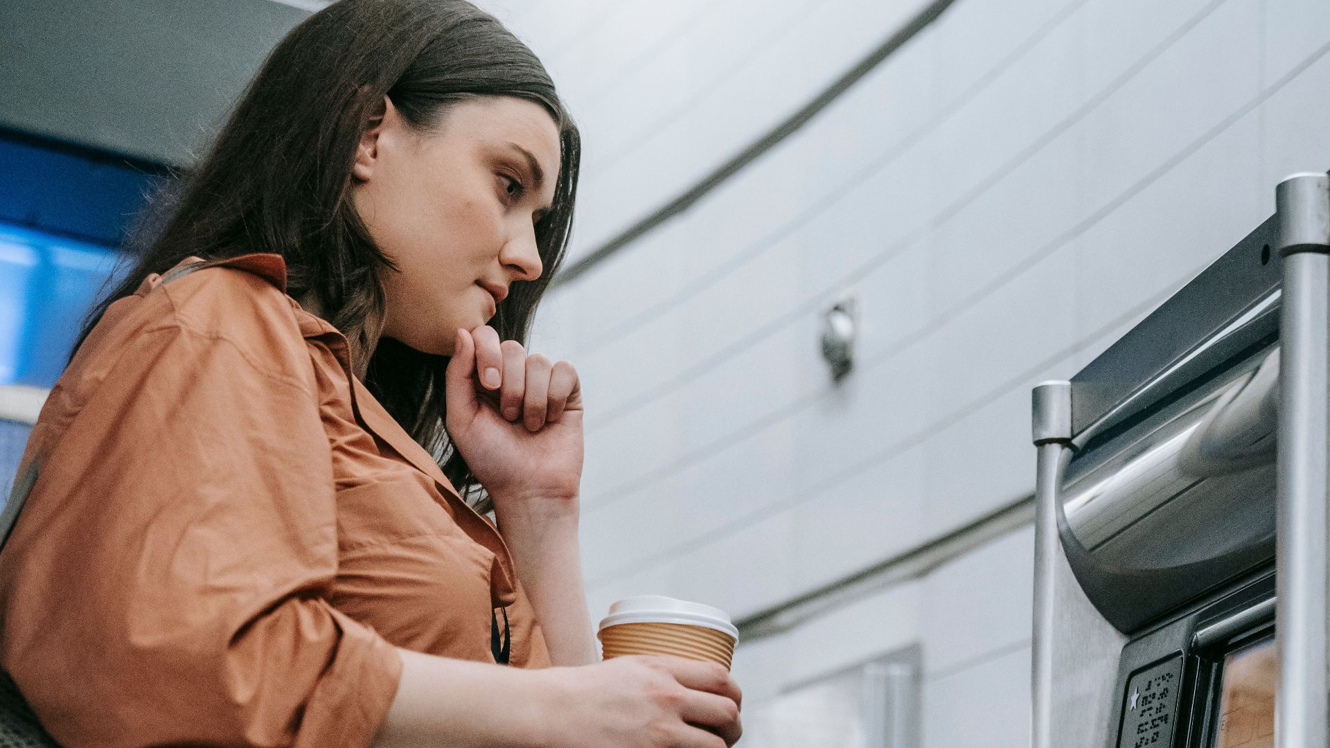 A young woman at a subway station uses a vending machine to purchase a ticket.
