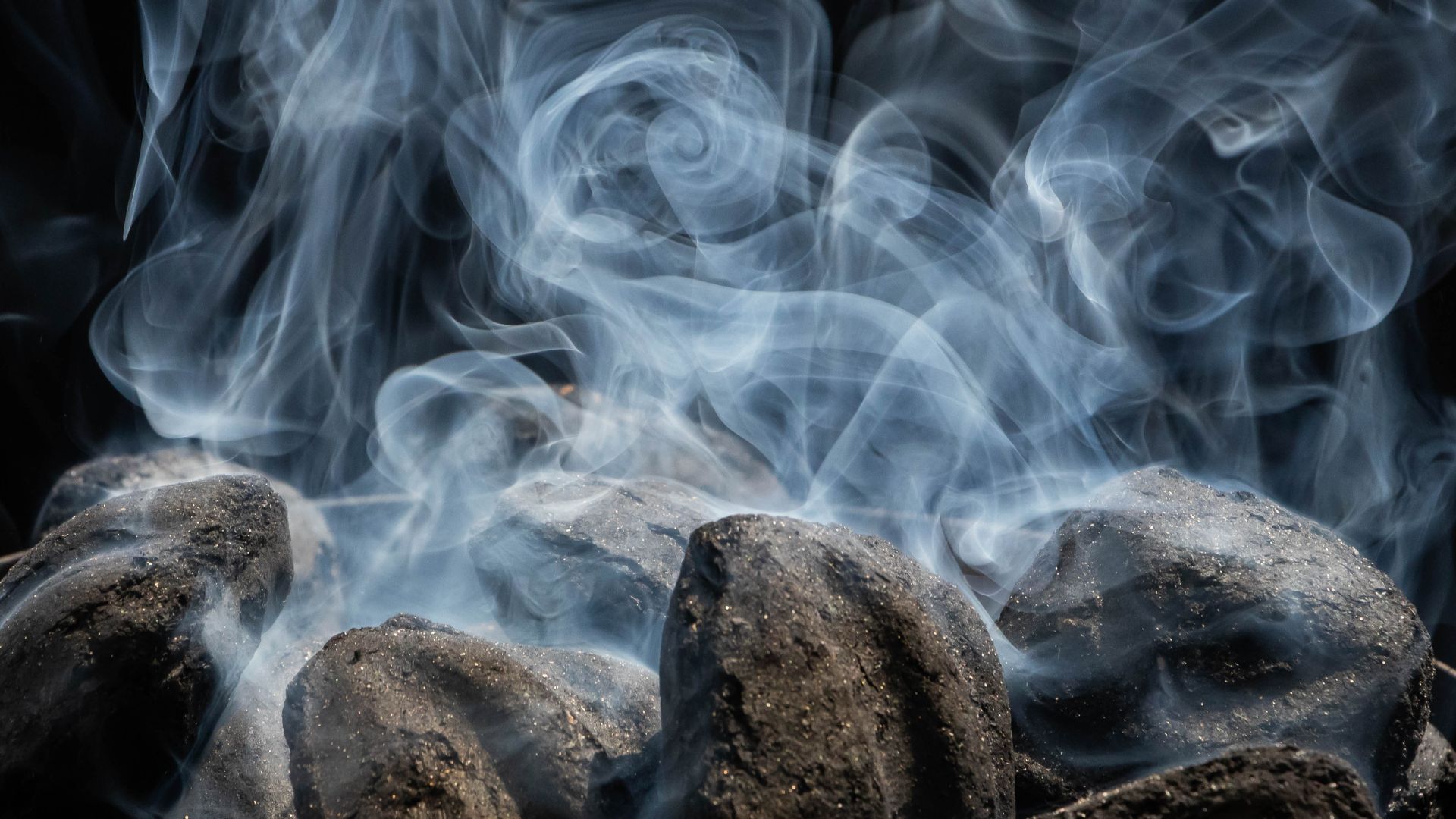White smoke rising from charcoal briquettes as they start to catch fire and burn.