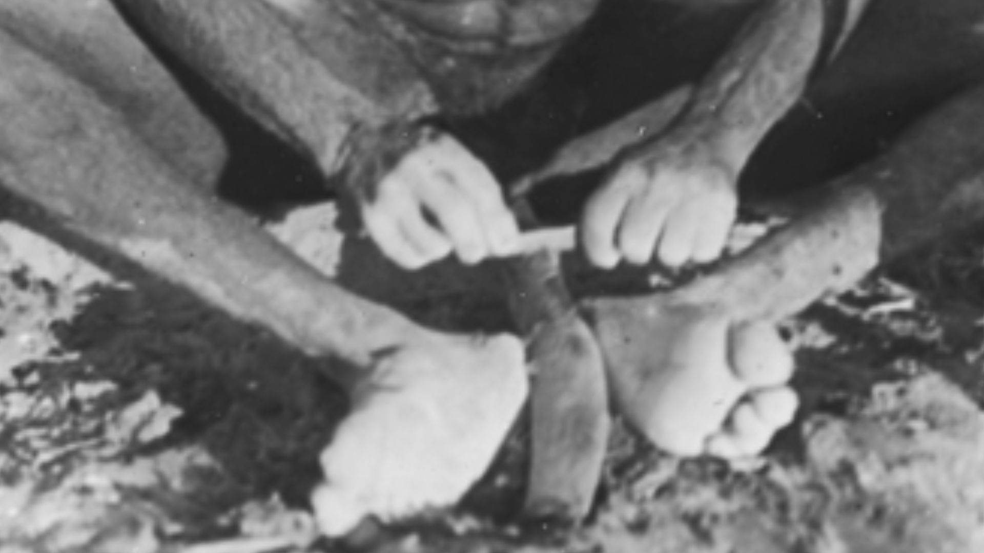 Man scraping a boomerang with a sharp stone flake.
