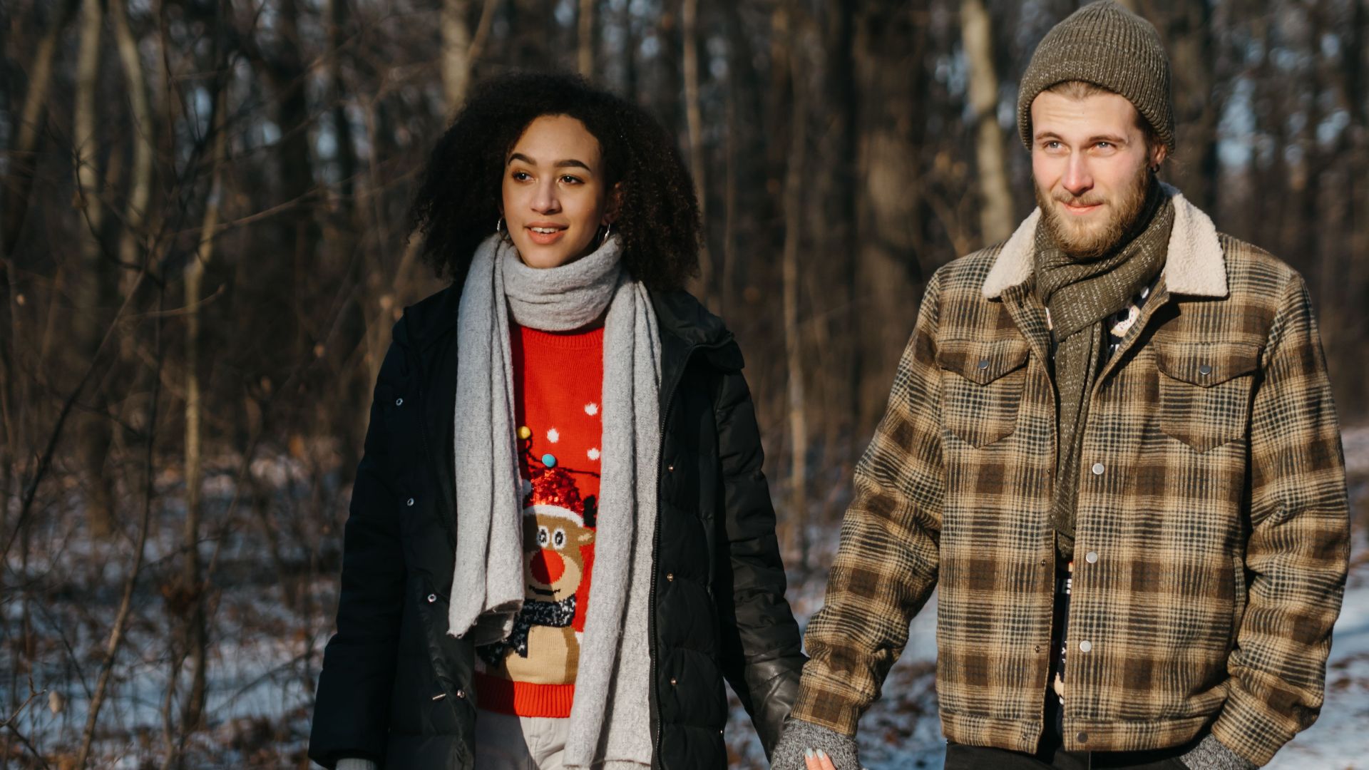 Interracial couple enjoying a winter walk, radiating love and happiness in festive attire.