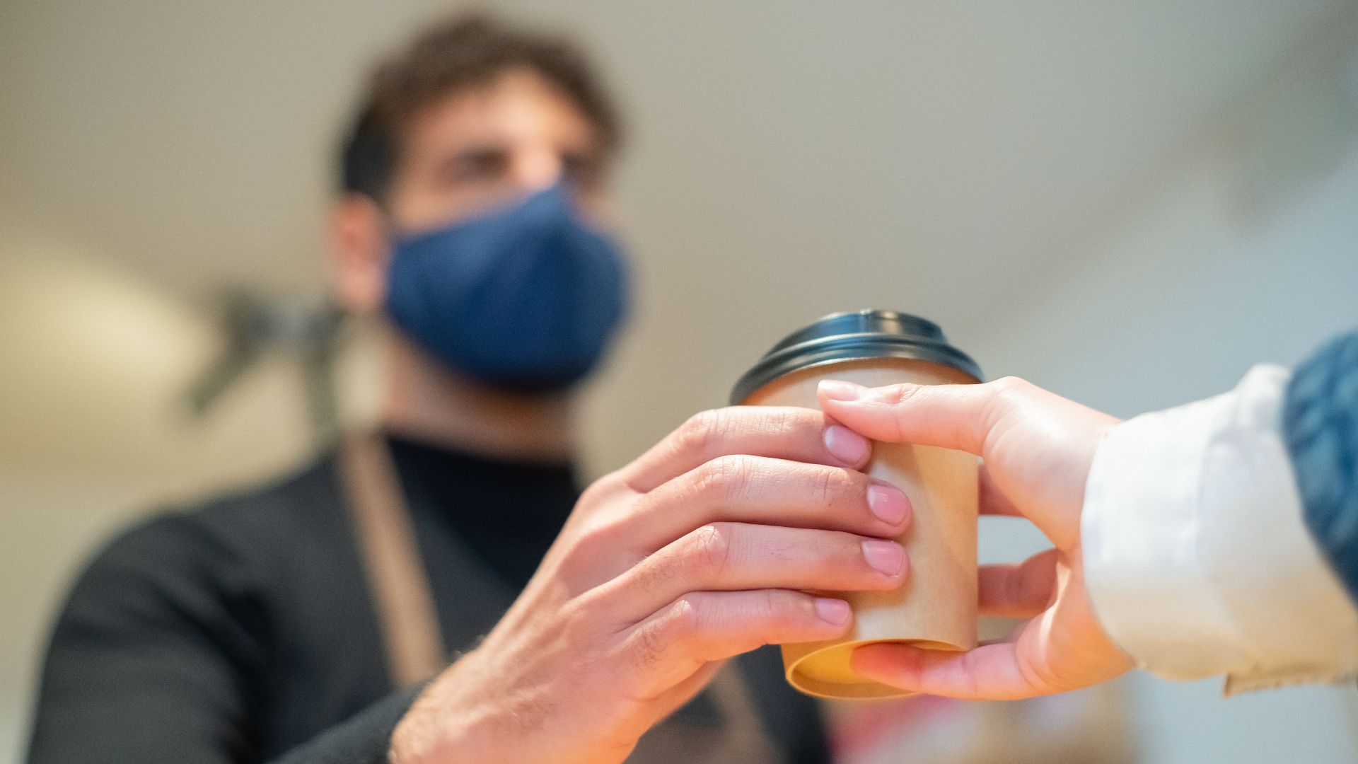 Barista hands over a to-go coffee cup with a focus on hand hygiene and service.
