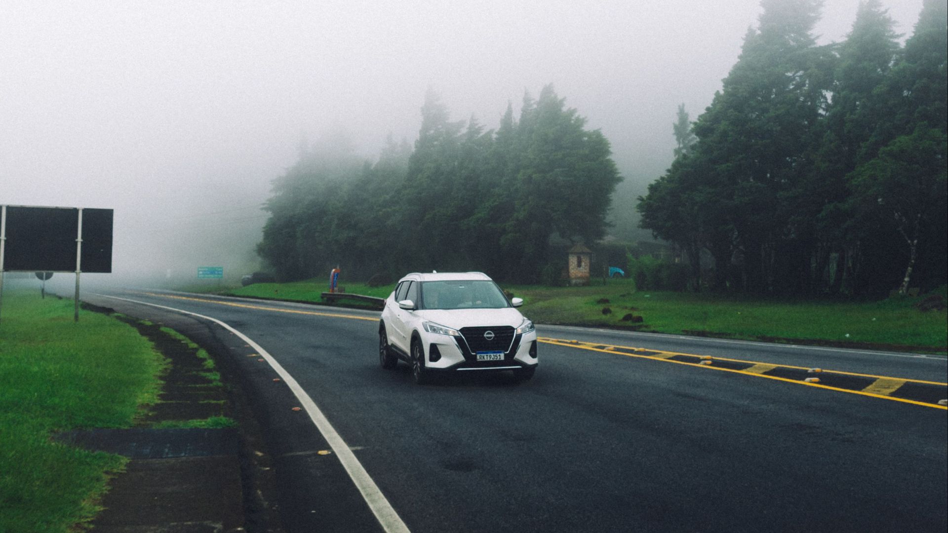 A white SUV travels through a foggy rural road surrounded by trees, creating a mysterious atmosphere.