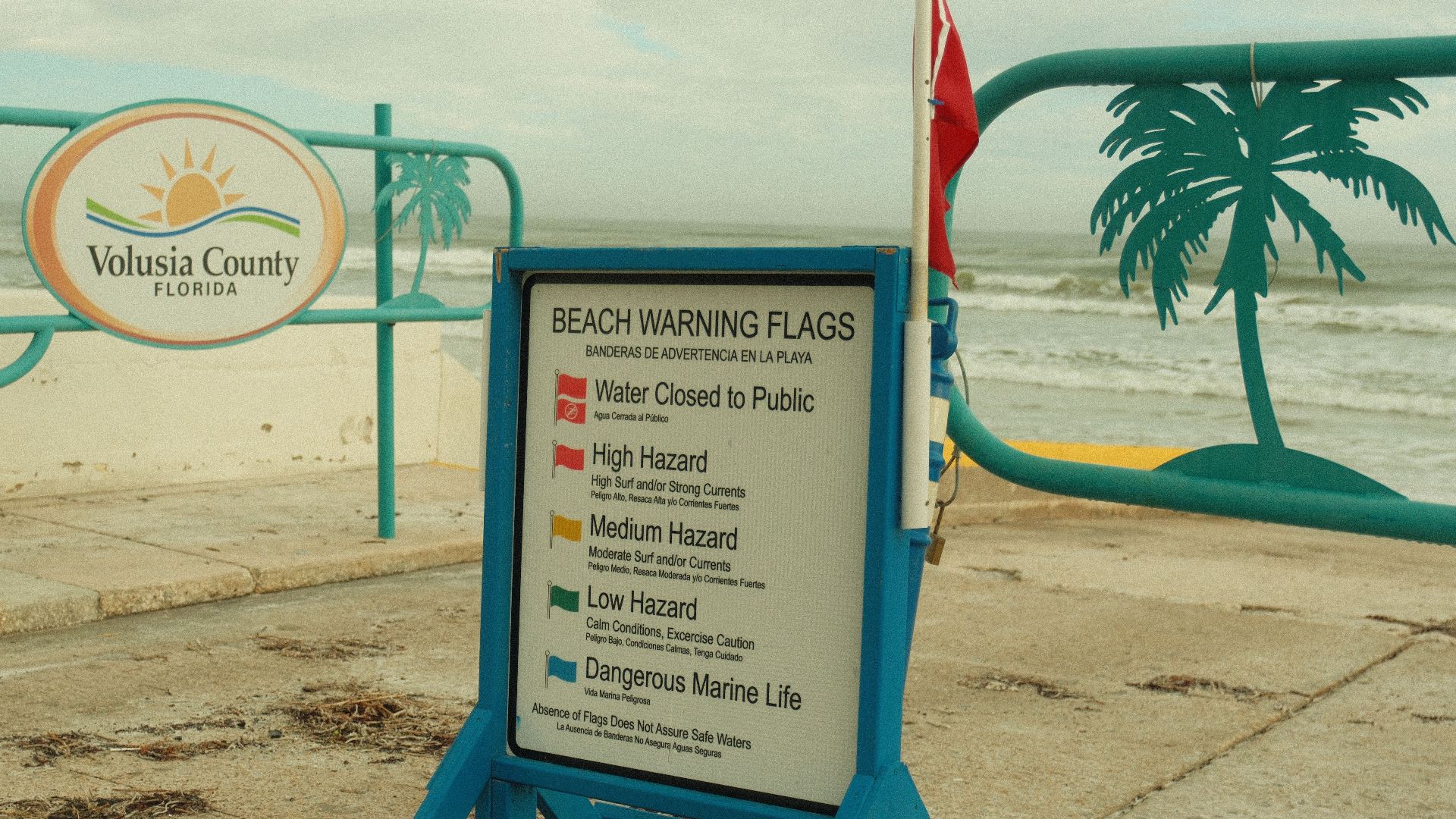 Beach warning flags sign in Volusia County, Florida, indicating hazard levels near public beach.