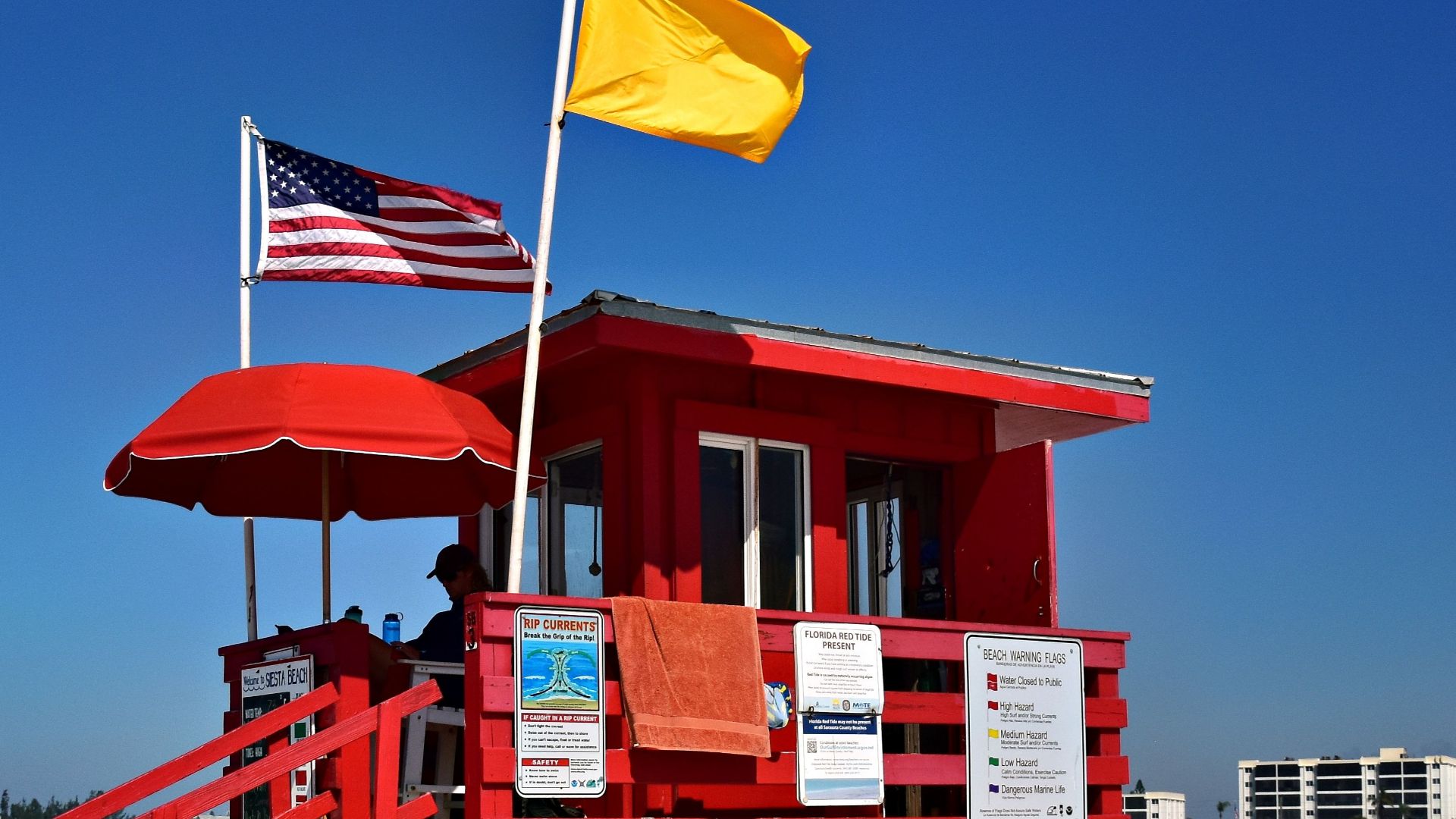 Bright red lifeguard tower with flags on a busy, sunlit beach, perfect for vacation scenery.