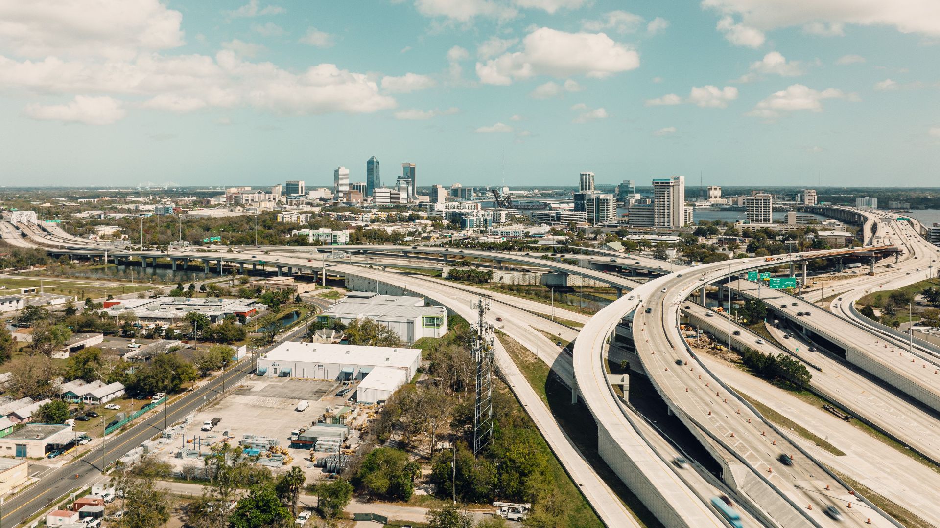 Drone shot of Jacksonville, FL skyline with complex highway network and bright sky.