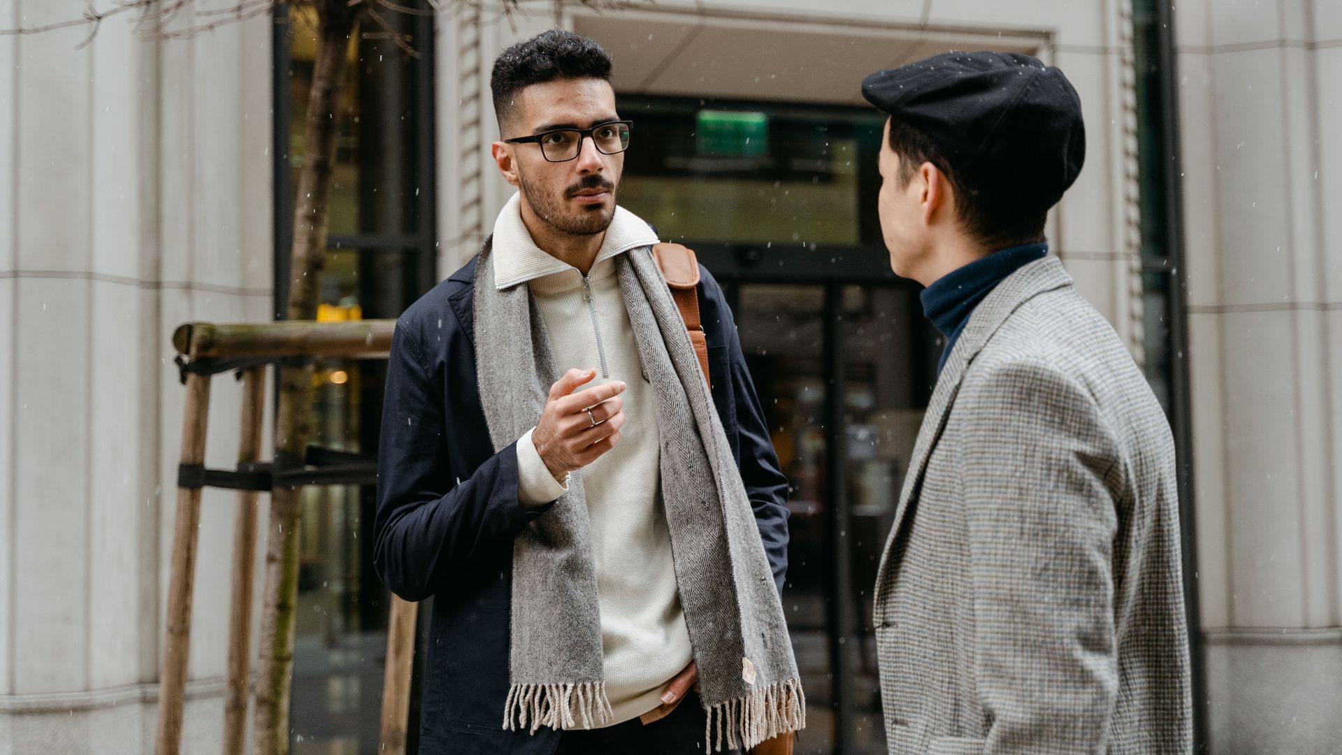 Two businessmen engaged in conversation outside in winter attire with snow falling lightly.