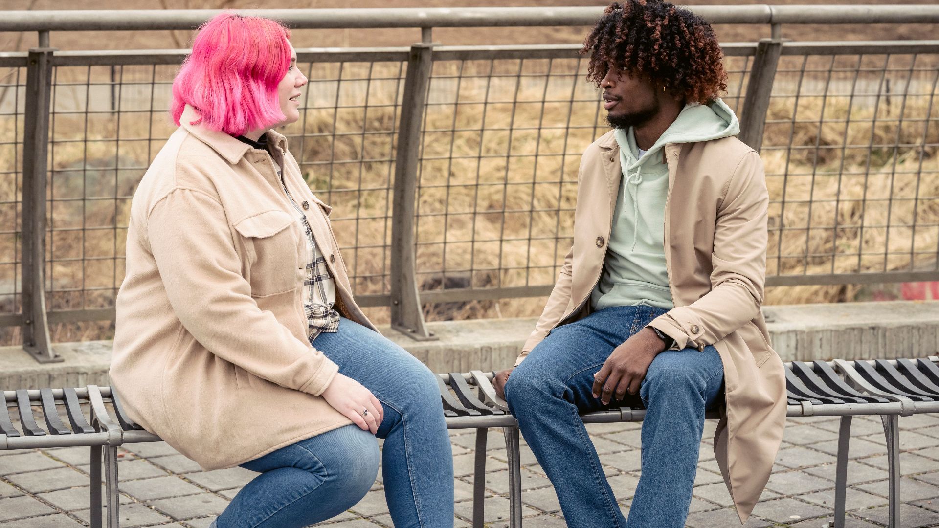 Two people having a conversation on a bench outdoors in a park setting.